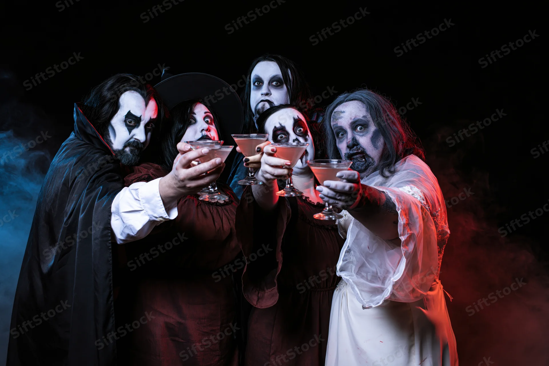 Five adults in halloween costumes toasting with cocktail glasses in a smoky dark setting