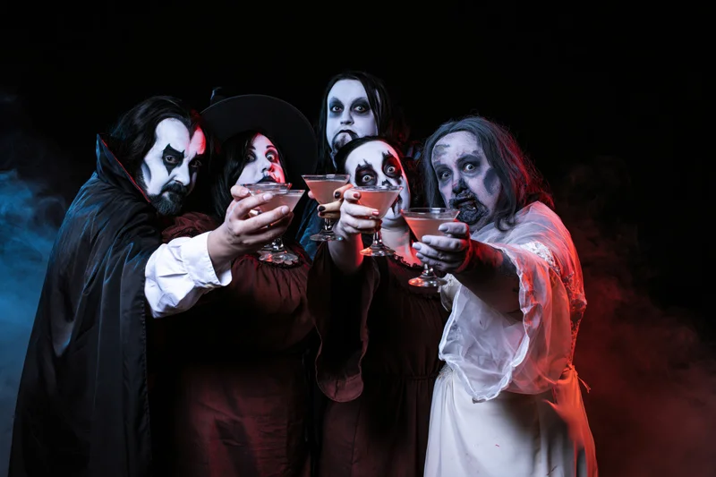Five adults in halloween costumes toasting with cocktail glasses in a smoky dark setting