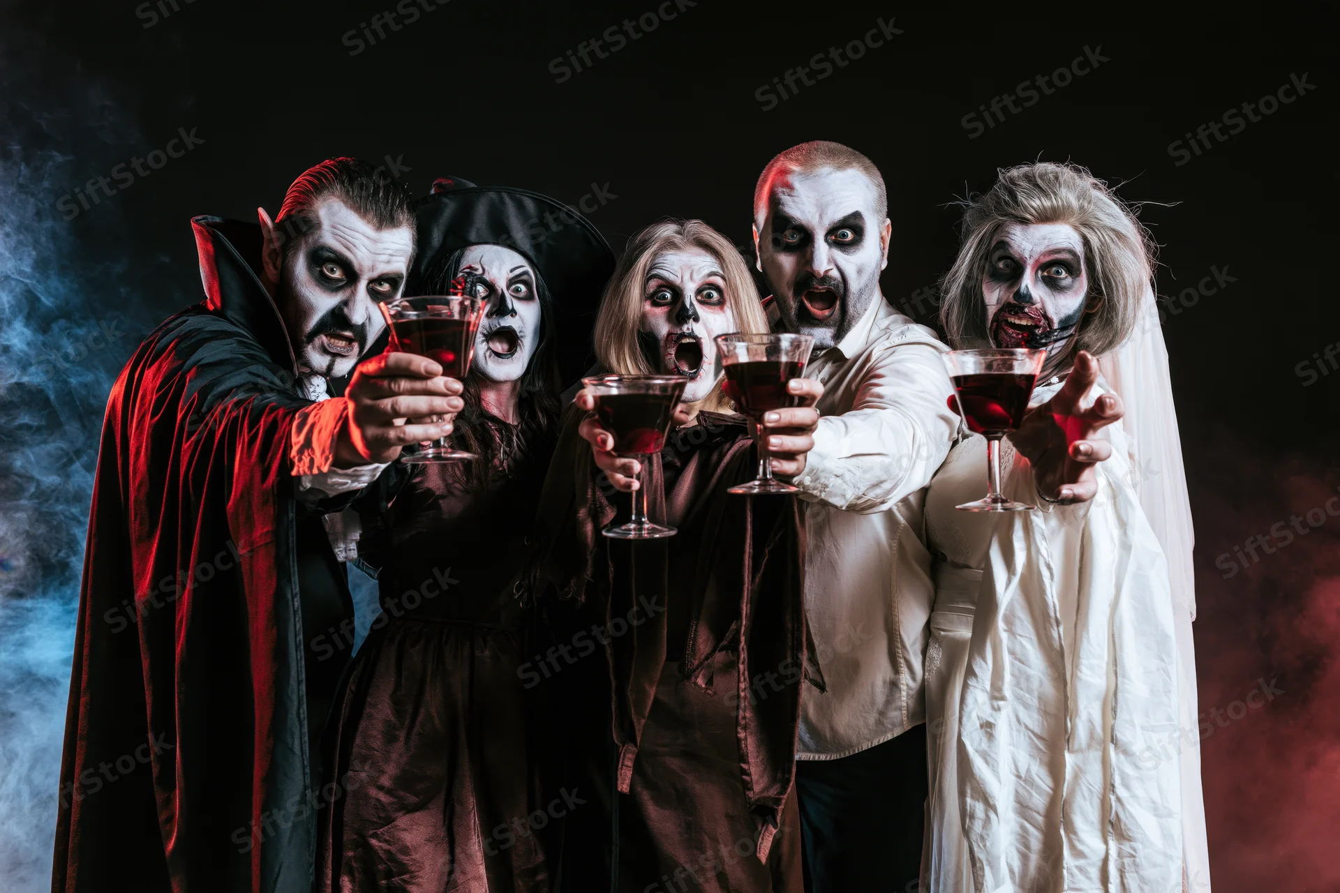 Five adults in vampire costumes holding cocktail glasses in a smoky dark setting for a halloween party