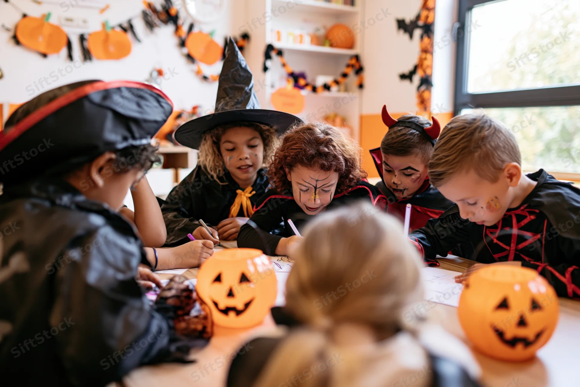 Children in halloween costumes writing at a classroom table during a school party