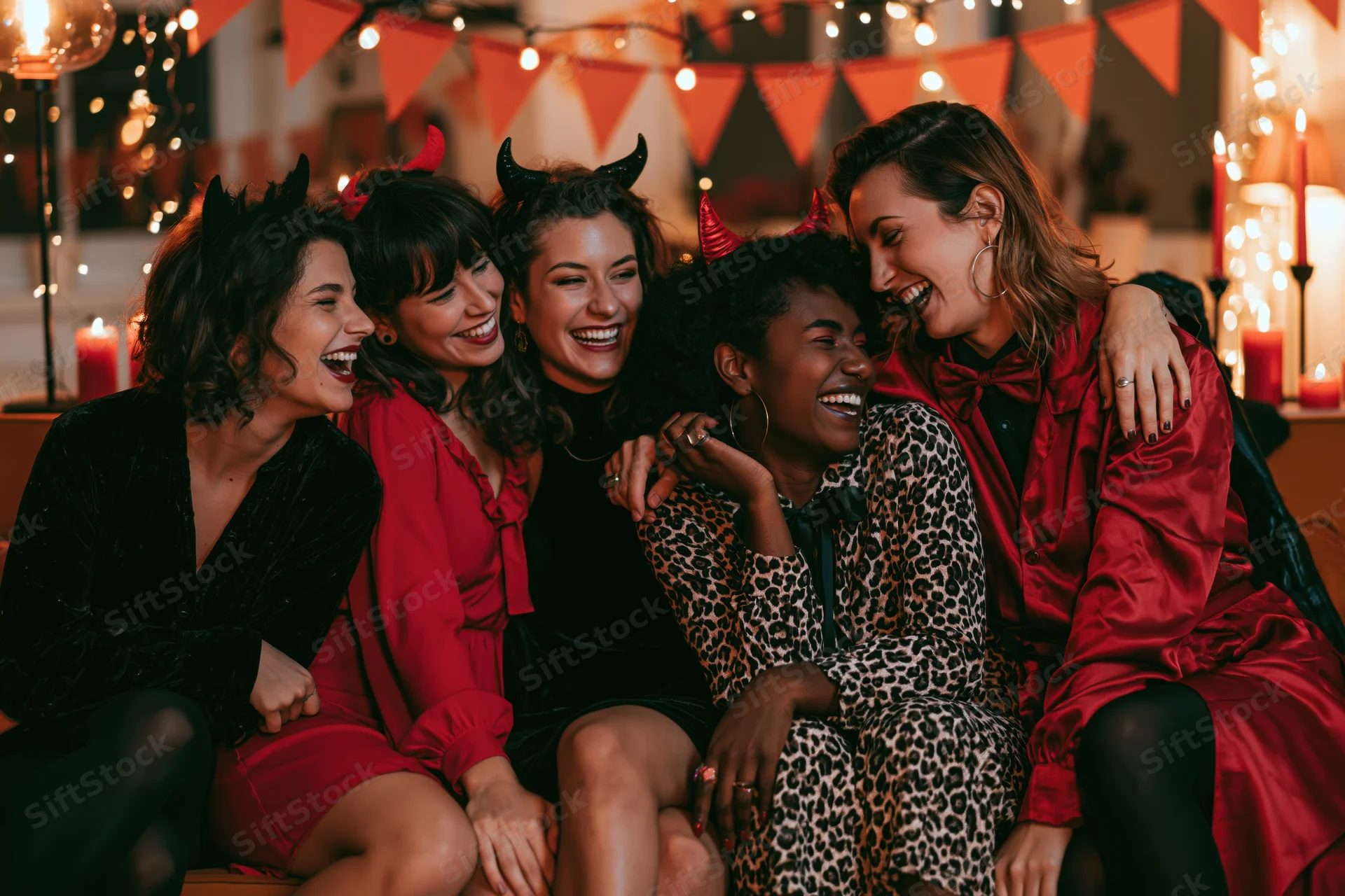 Five women in halloween costumes laughing together indoors at a decorated party