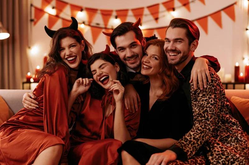 Five friends in halloween costumes laughing together on a couch in a decorated living room