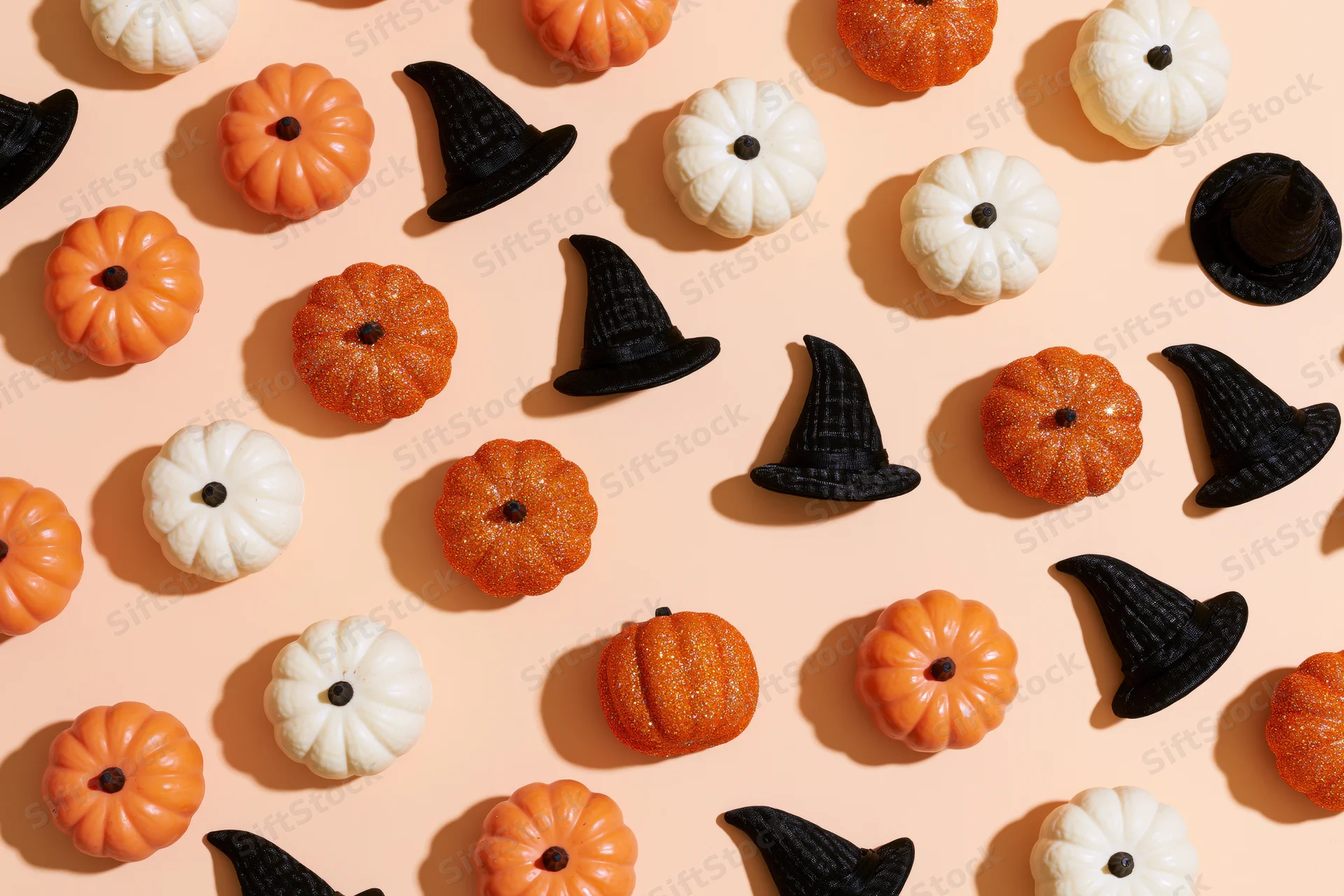 Small decorative pumpkins and witch hats arranged in a flat lay on a peach background
