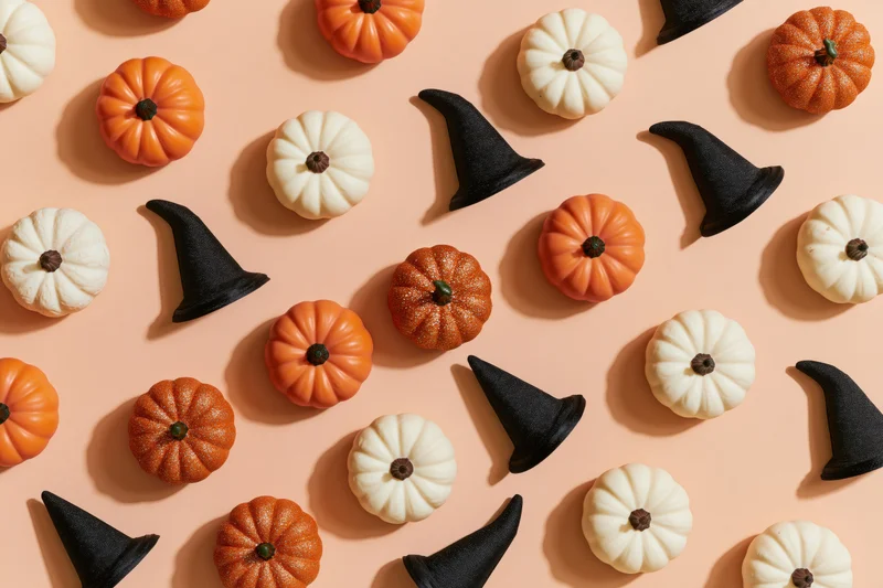 Small decorative pumpkins and witch hats arranged in a flat lay on a peach background