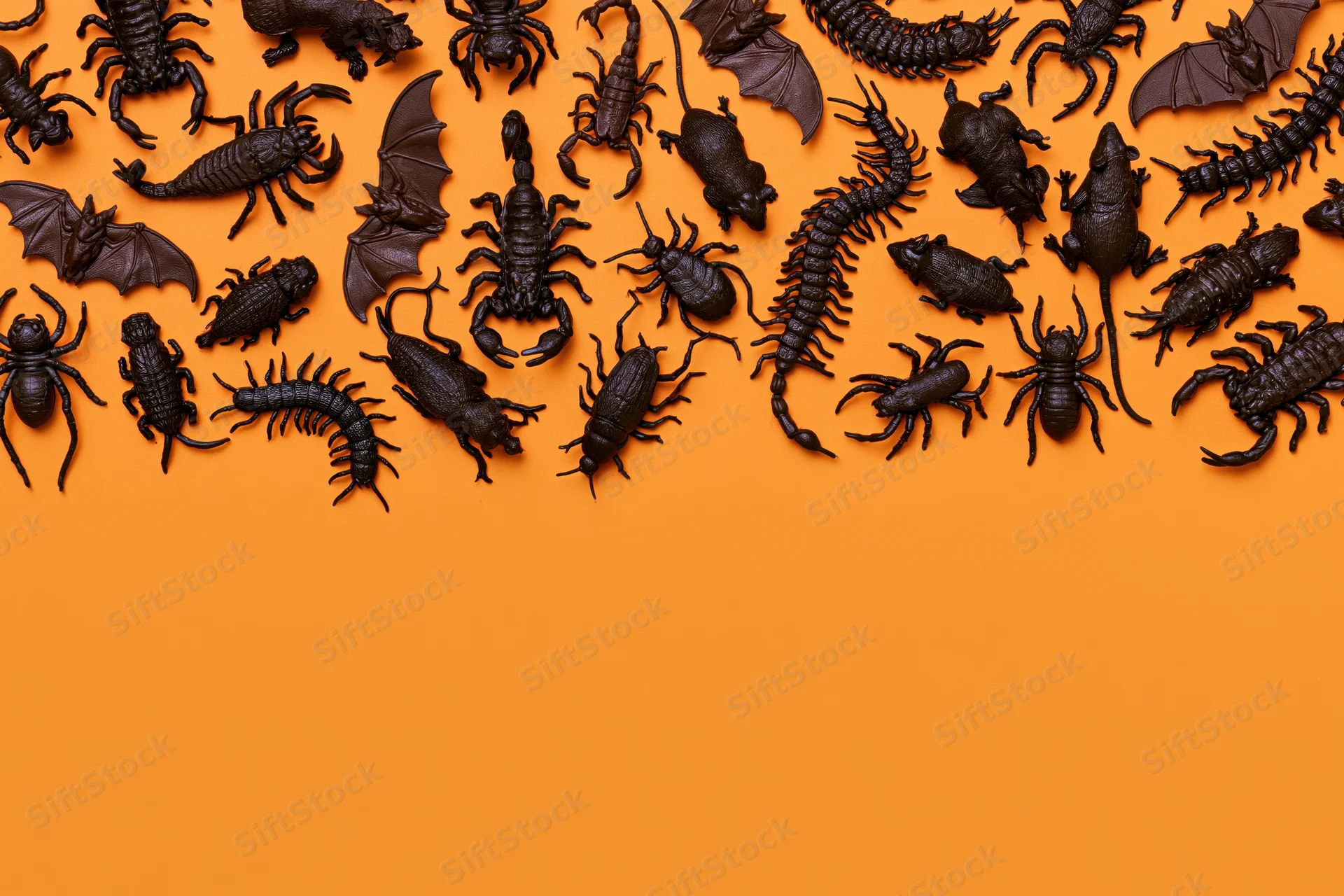 Dark plastic halloween toy creatures arranged in flat lay on orange surface with copyspace below