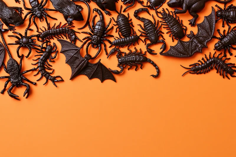 Dark plastic halloween toy creatures arranged on orange surface with copyspace
