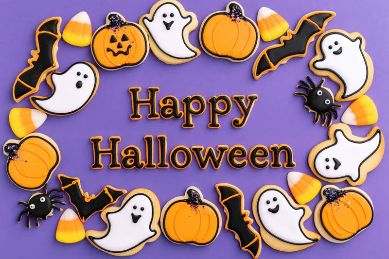 Decorated halloween sugar cookies arranged in a circular frame around happy halloween text on purple background