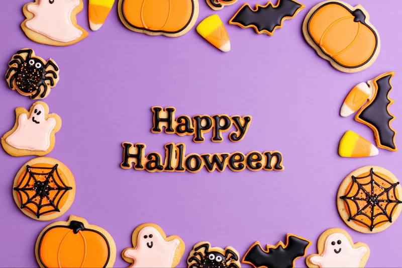 Decorated halloween sugar cookies arranged in a frame on purple background with happy halloween text and copyspace