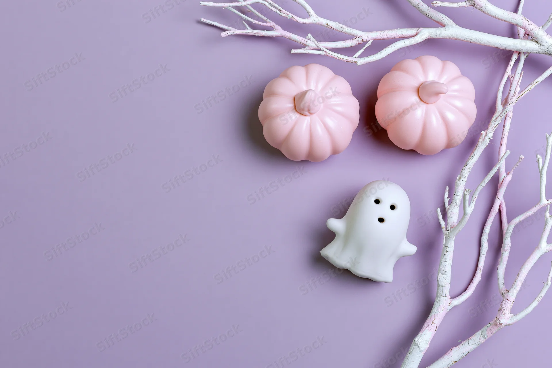 Two pink ceramic pumpkins and a white ghost ornament arranged with painted branches on a purple surface