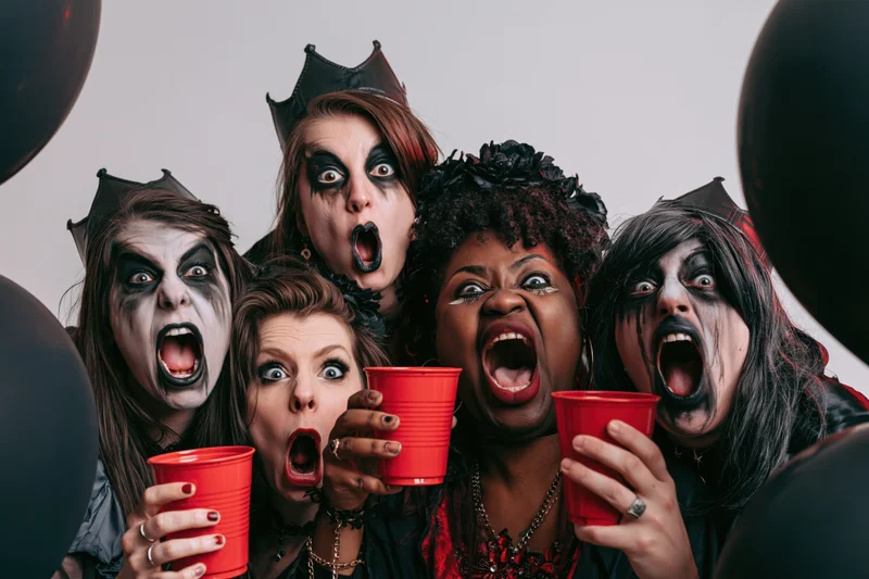 Women in halloween costumes with theatrical makeup screaming while holding red cups at a party