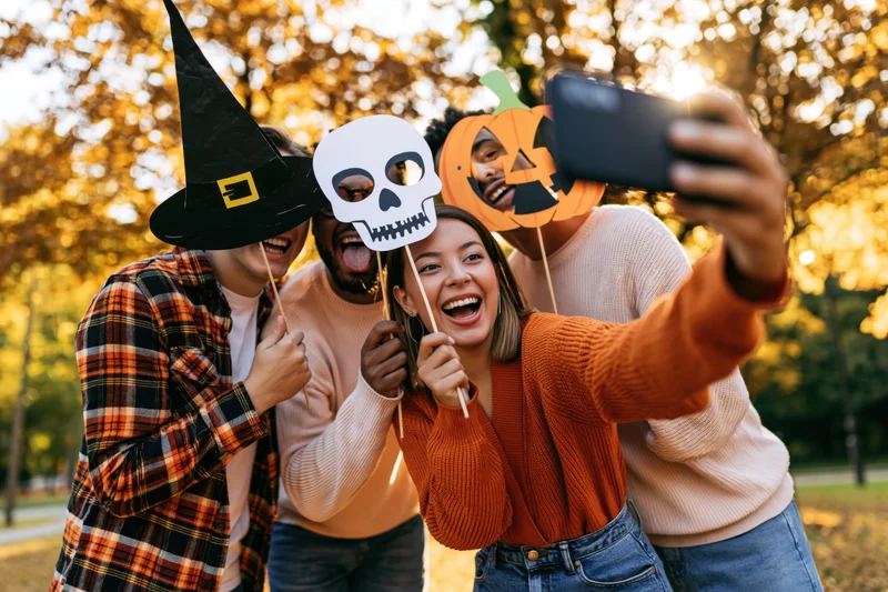 Four friends taking a group selfie outdoors with halloween props in a park during autumn