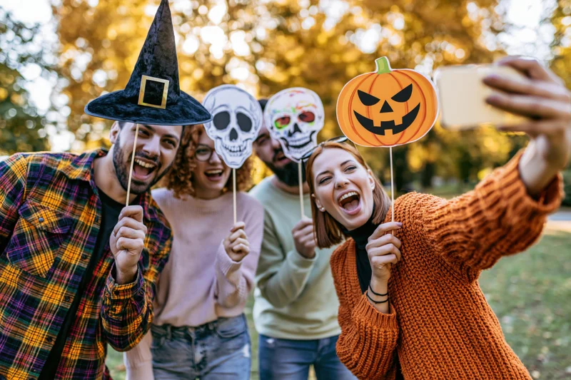 Four friends taking a group selfie outdoors with halloween props in a park during autumn