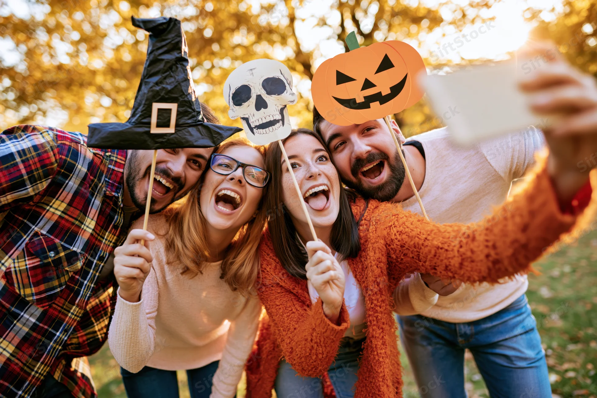 Four friends taking a group selfie outdoors with halloween props in autumn foliage