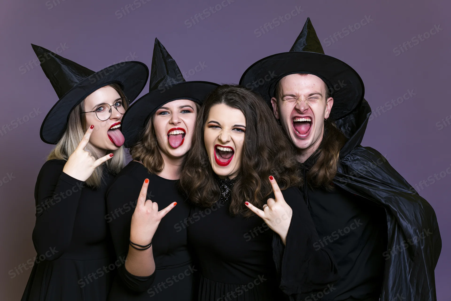 Four young adults in witch and wizard costumes making playful faces and rock hand gestures in a studio setting