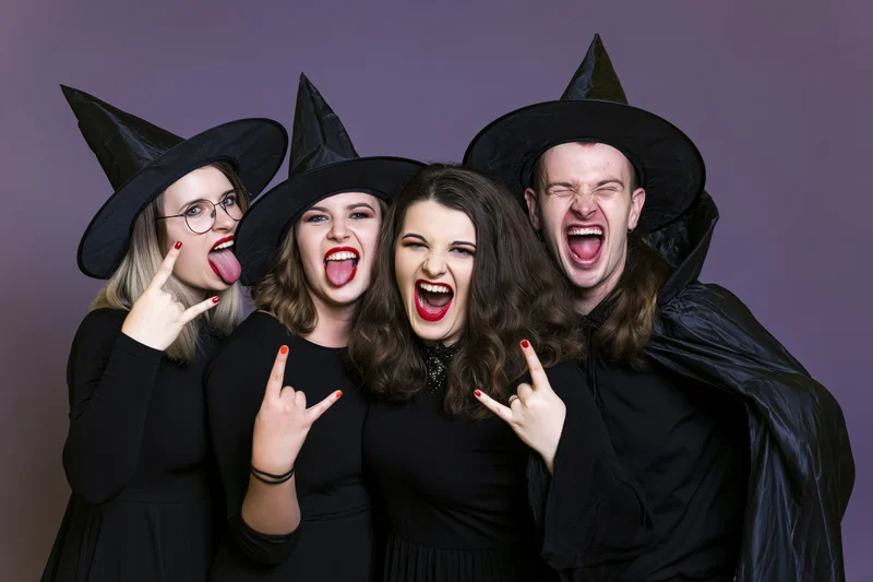 Four young adults in witch and wizard costumes making playful faces and rock hand gestures in a studio setting