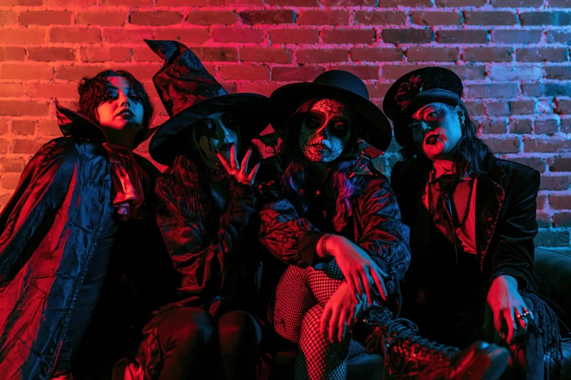 Four young women in halloween costumes posing together on a couch against a brick wall lit with red and blue neon lights