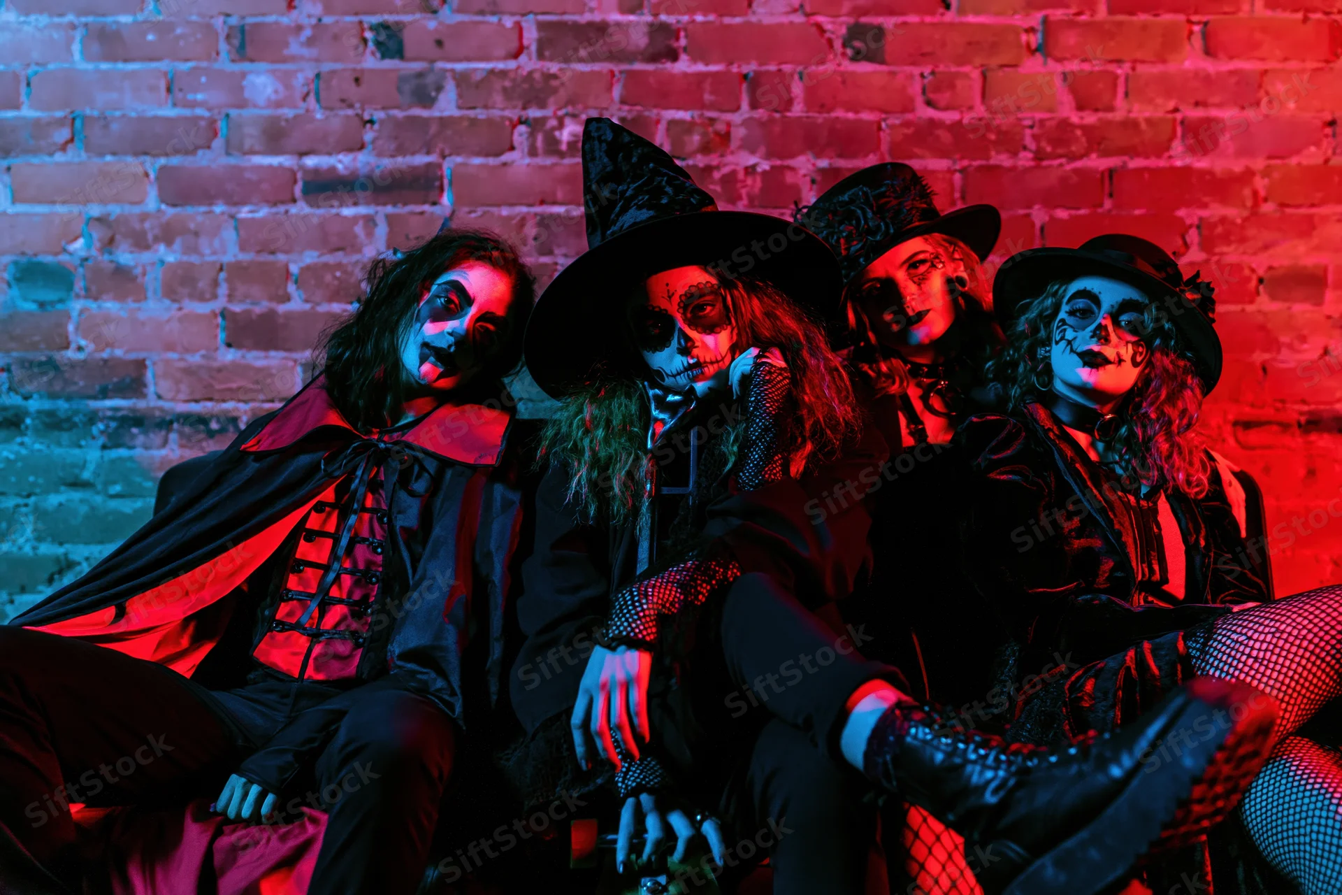 Four young adults in halloween costumes sitting together on a brick wall under red and blue lighting