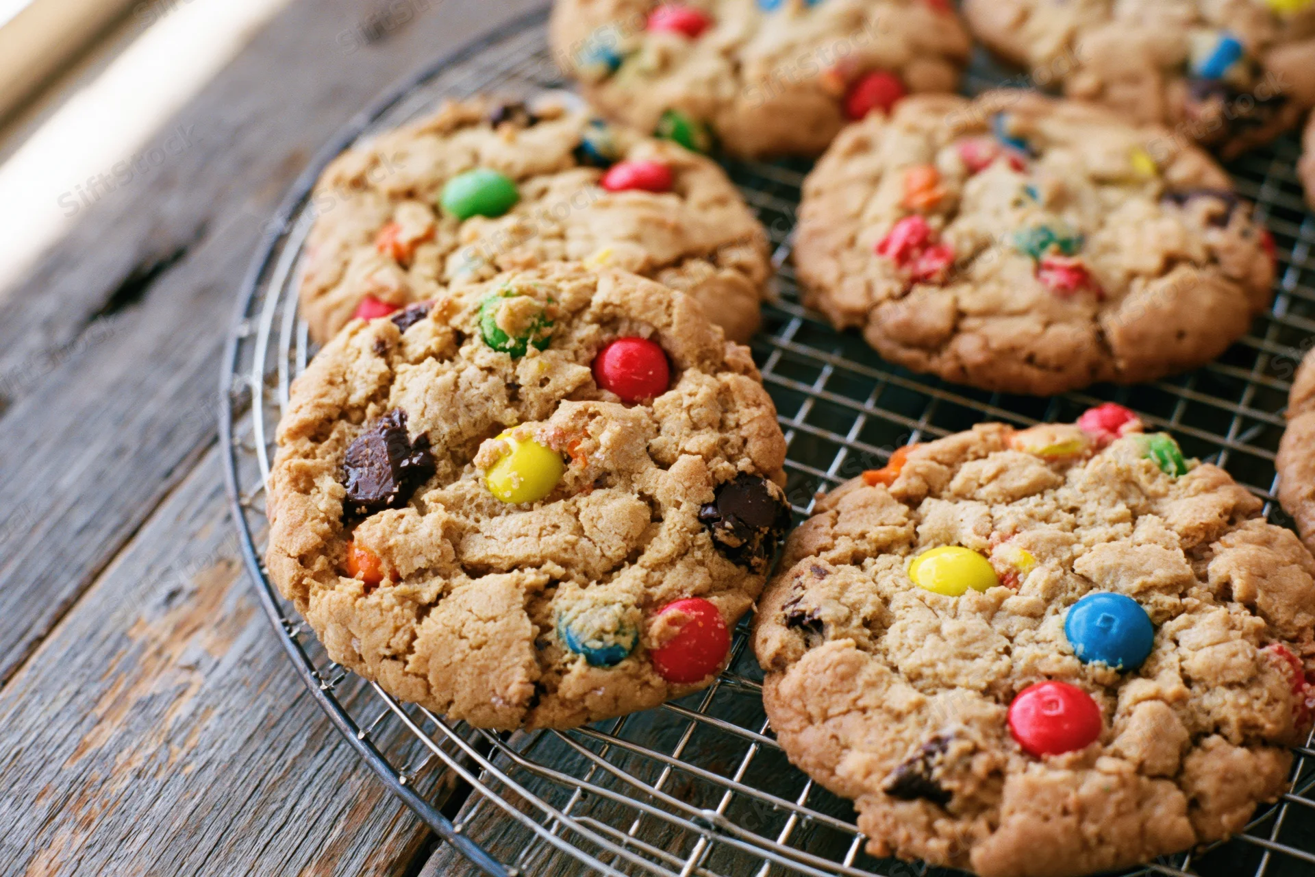 Freshly baked monster cookies with colorful candy and chocolate chips cooling on a wire rack on a wooden table