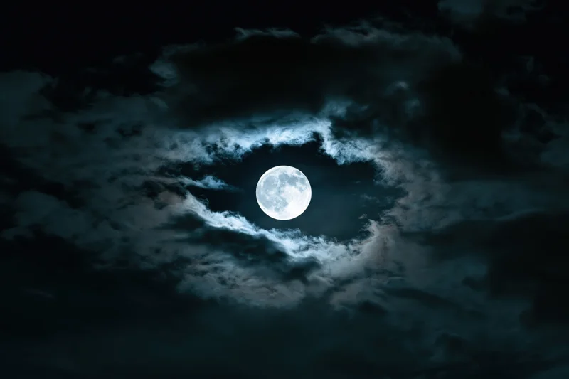 Full moon glowing through swirling clouds in a dark night sky