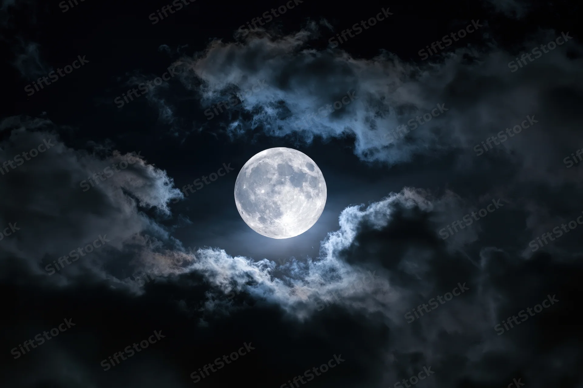 Full moon centered in dramatic night sky partially surrounded by dark clouds