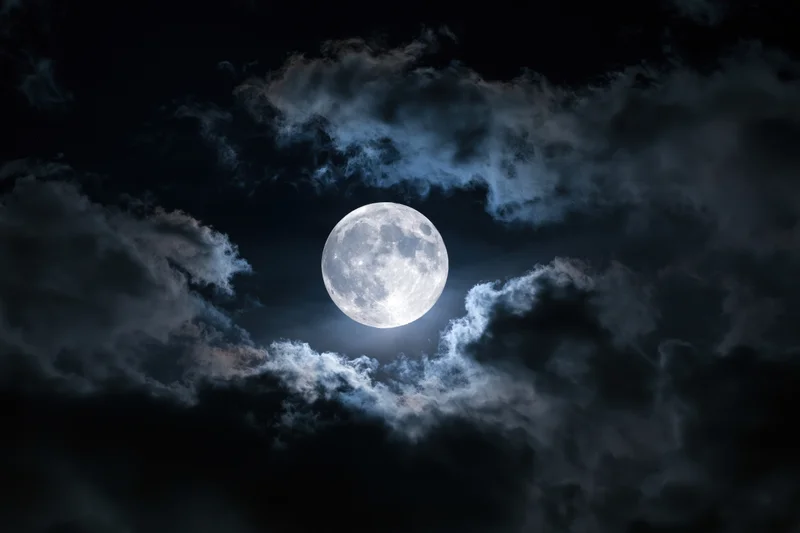 Full moon centered in dramatic night sky partially surrounded by dark clouds