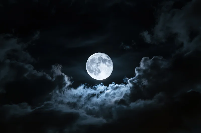 Full moon centered in a dramatic night sky partially surrounded by clouds