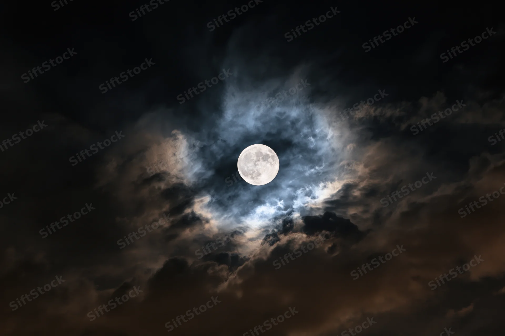 Full moon centered in turbulent night sky surrounded by swirling clouds