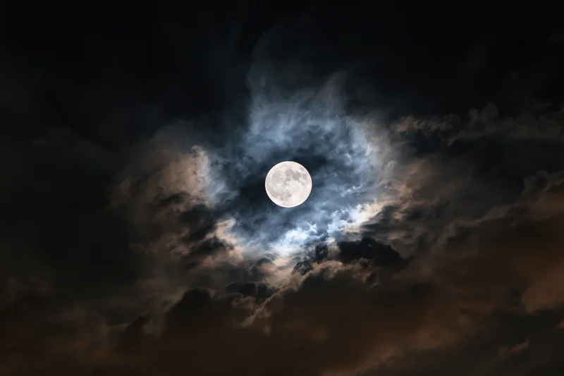 Full moon centered in turbulent night sky surrounded by swirling clouds