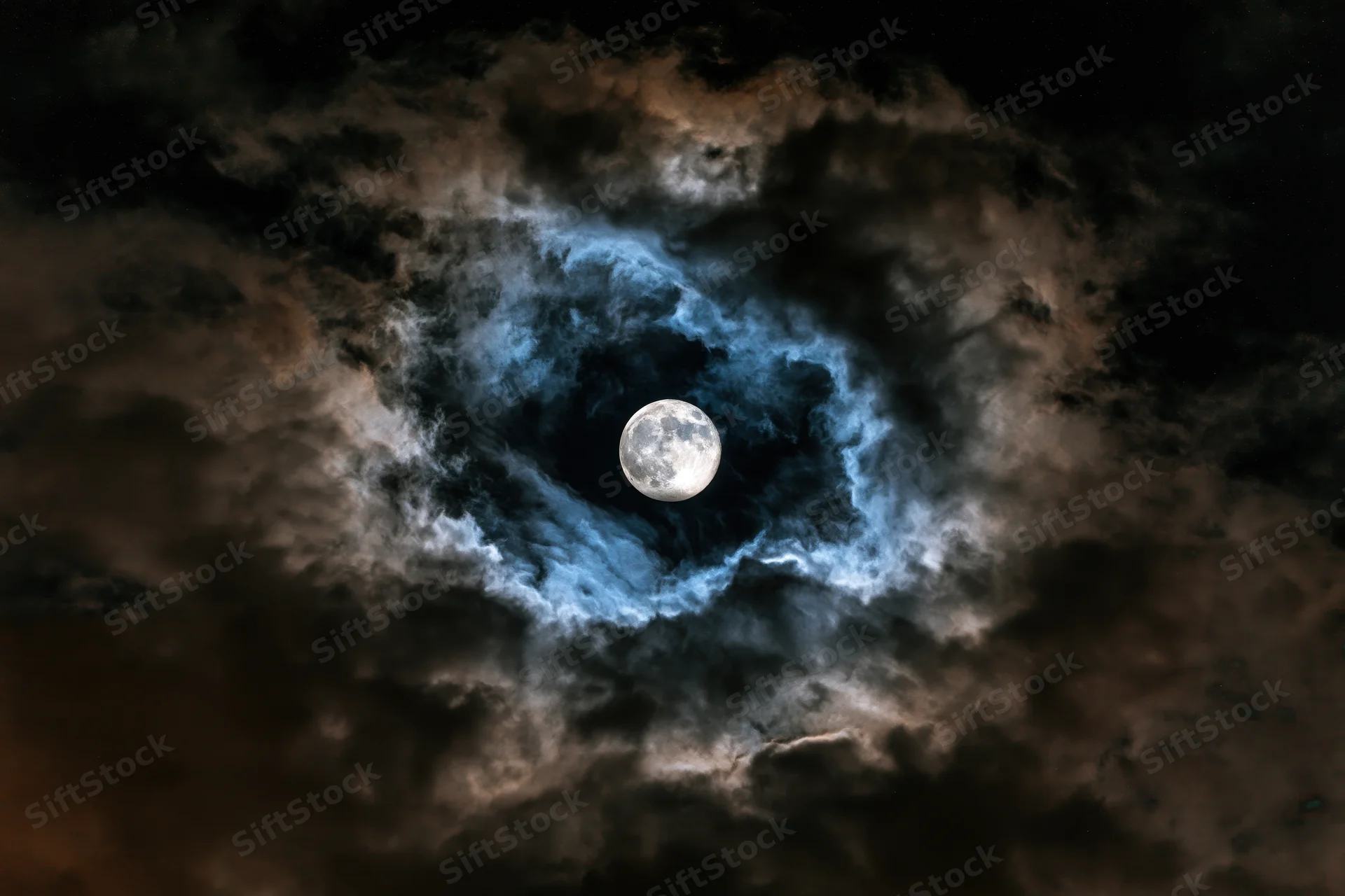 Full moon centered in turbulent night sky surrounded by swirling dark clouds