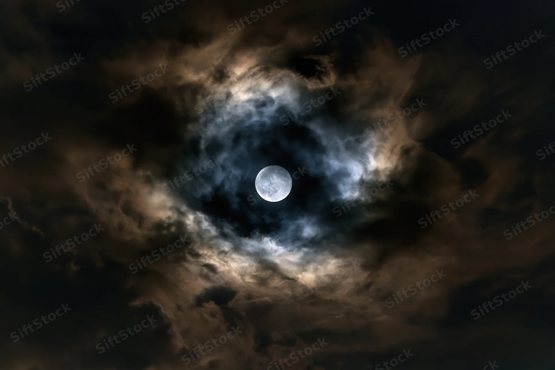 Full moon glowing in turbulent night sky surrounded by swirling clouds