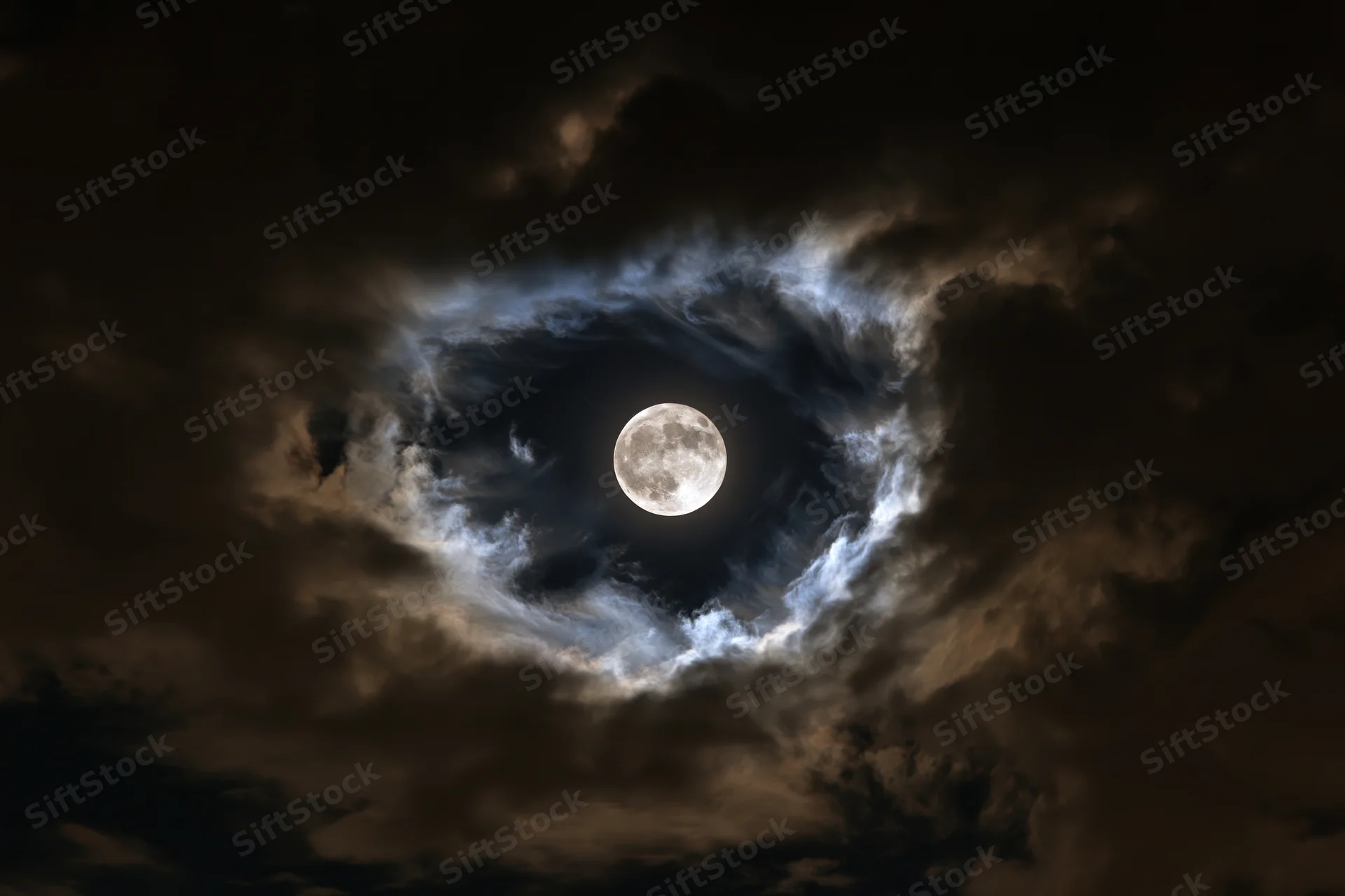 Full moon glowing in dark stormy sky surrounded by swirling clouds