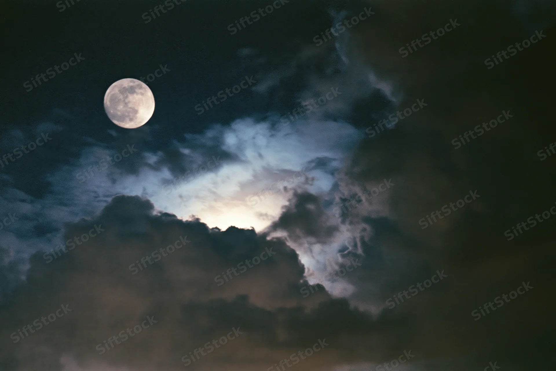 Full moon glowing through thick billowing clouds in the night sky