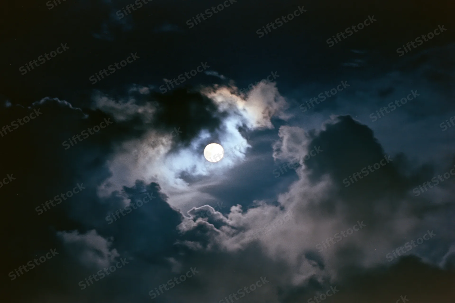 Full moon glowing through thick billowing clouds at night
