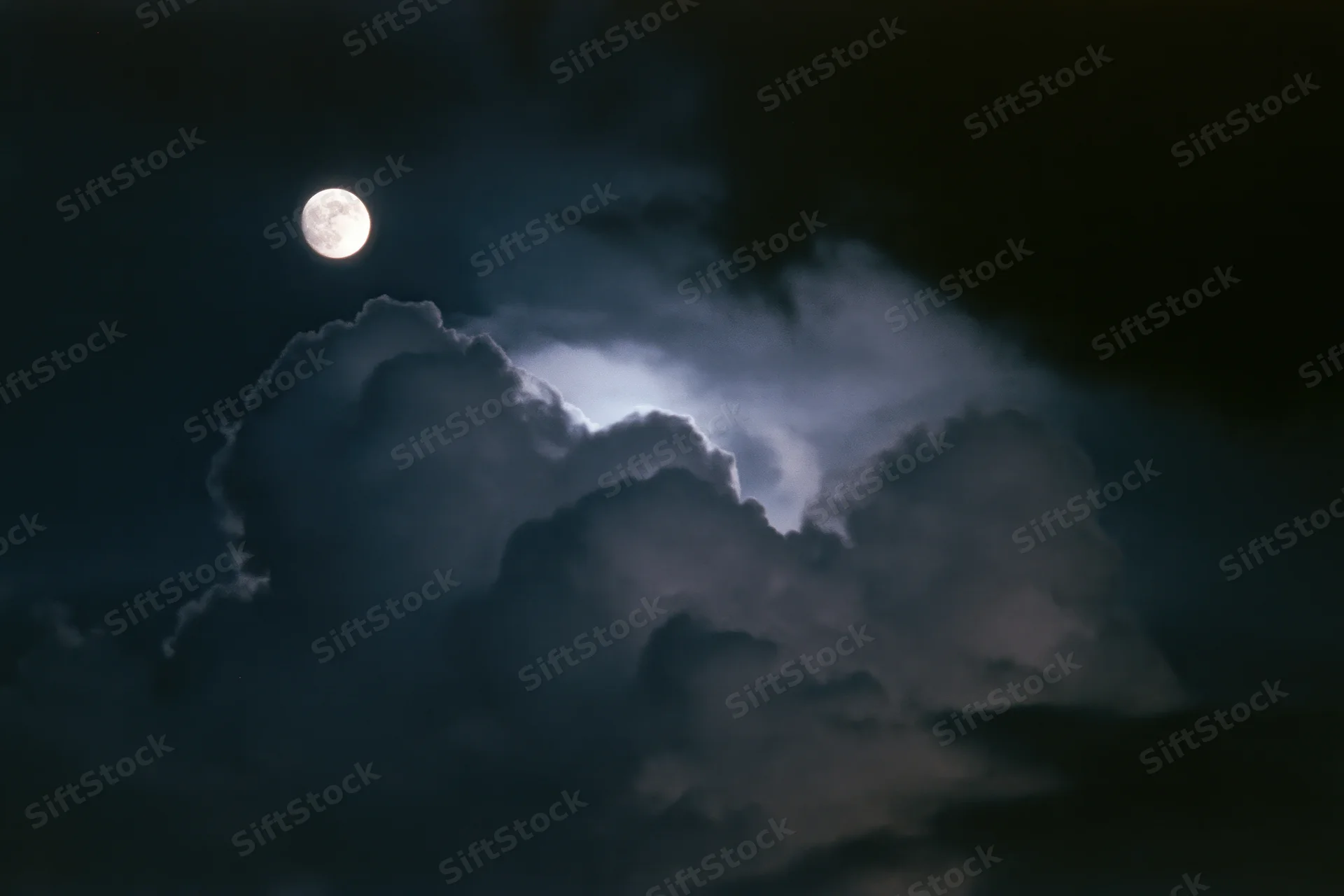 Full moon glowing above thick billowing clouds in the night sky