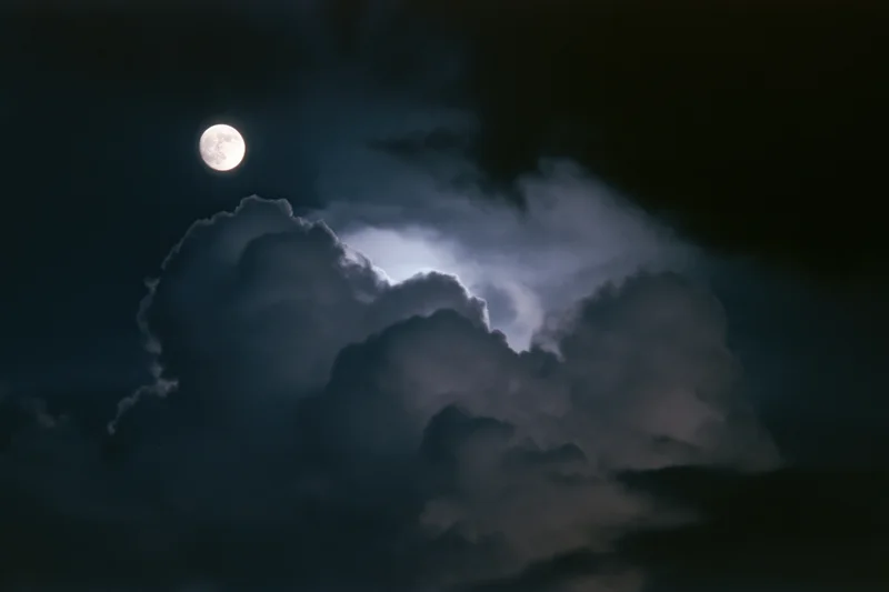 Full moon glowing above thick billowing clouds in the night sky