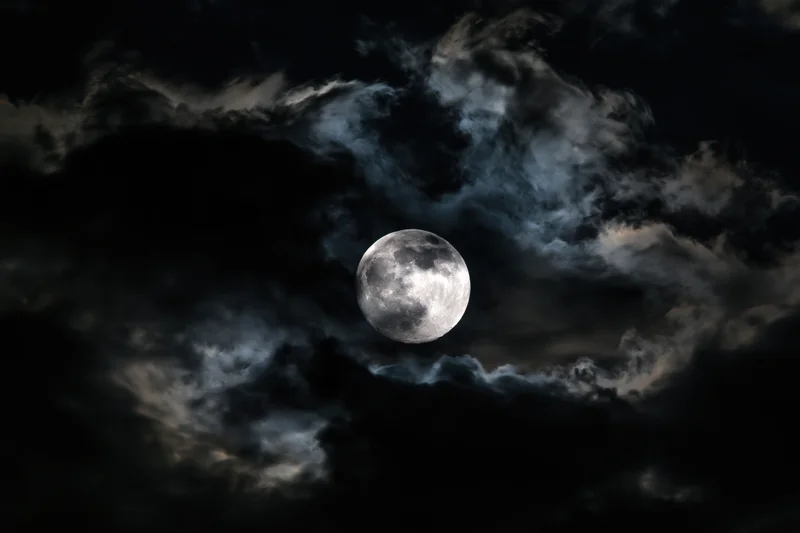Full moon glowing through swirling storm clouds in dark night sky