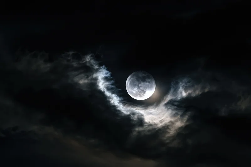 Full moon glowing through swirling storm clouds in the night sky