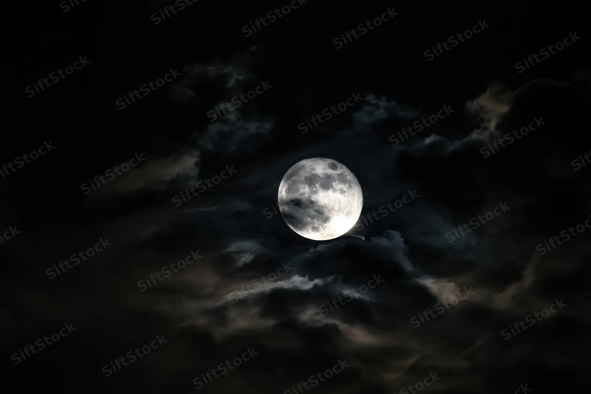 Full moon glowing through churning storm clouds in dark night sky