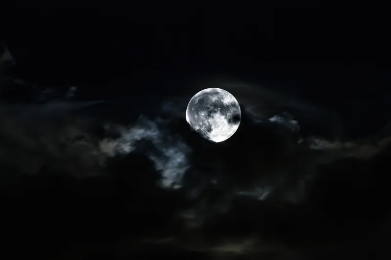 Full moon glowing through churning storm clouds in dark night sky