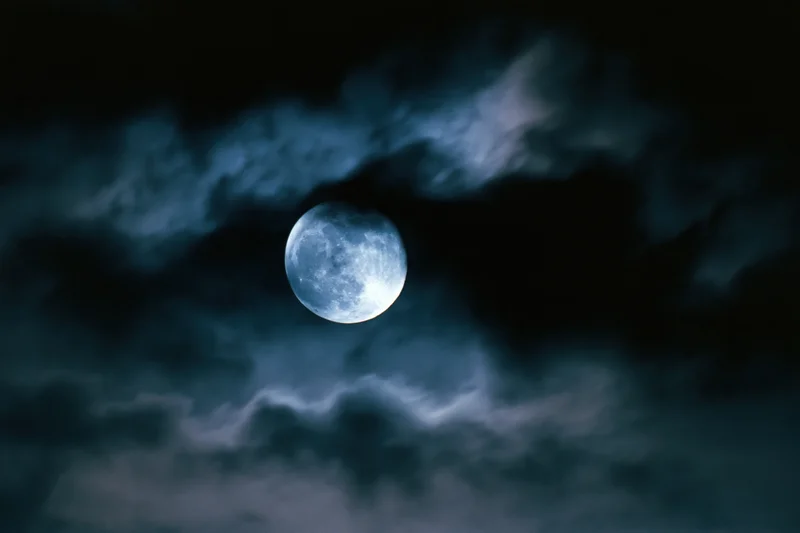 Full moon glowing through drifting dark clouds in the night sky