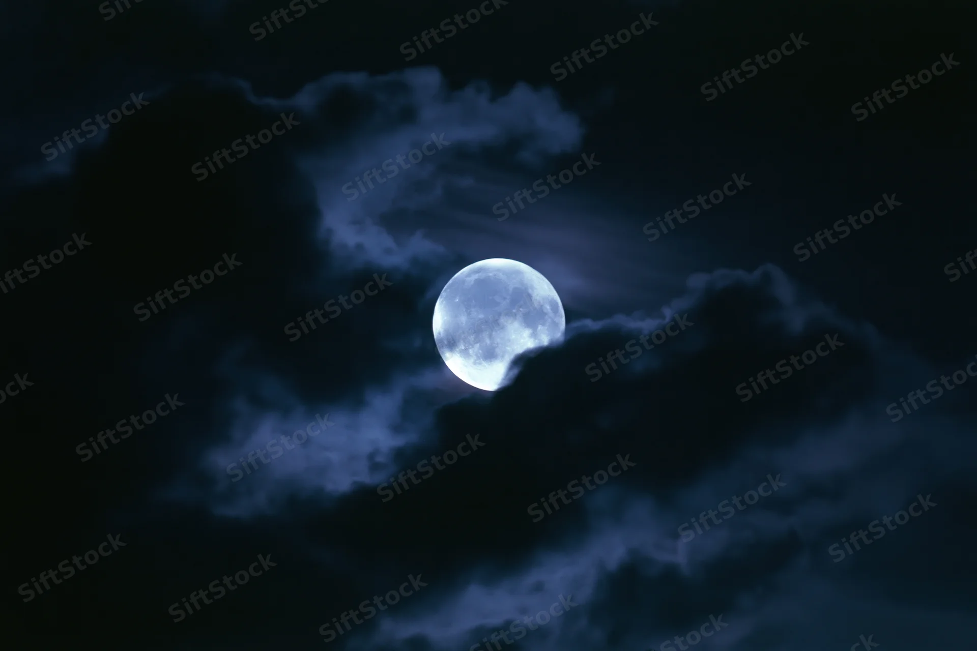 Full moon glowing through drifting dark clouds in the night sky