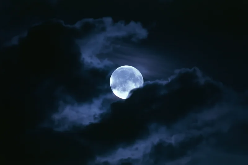 Full moon glowing through drifting dark clouds in the night sky