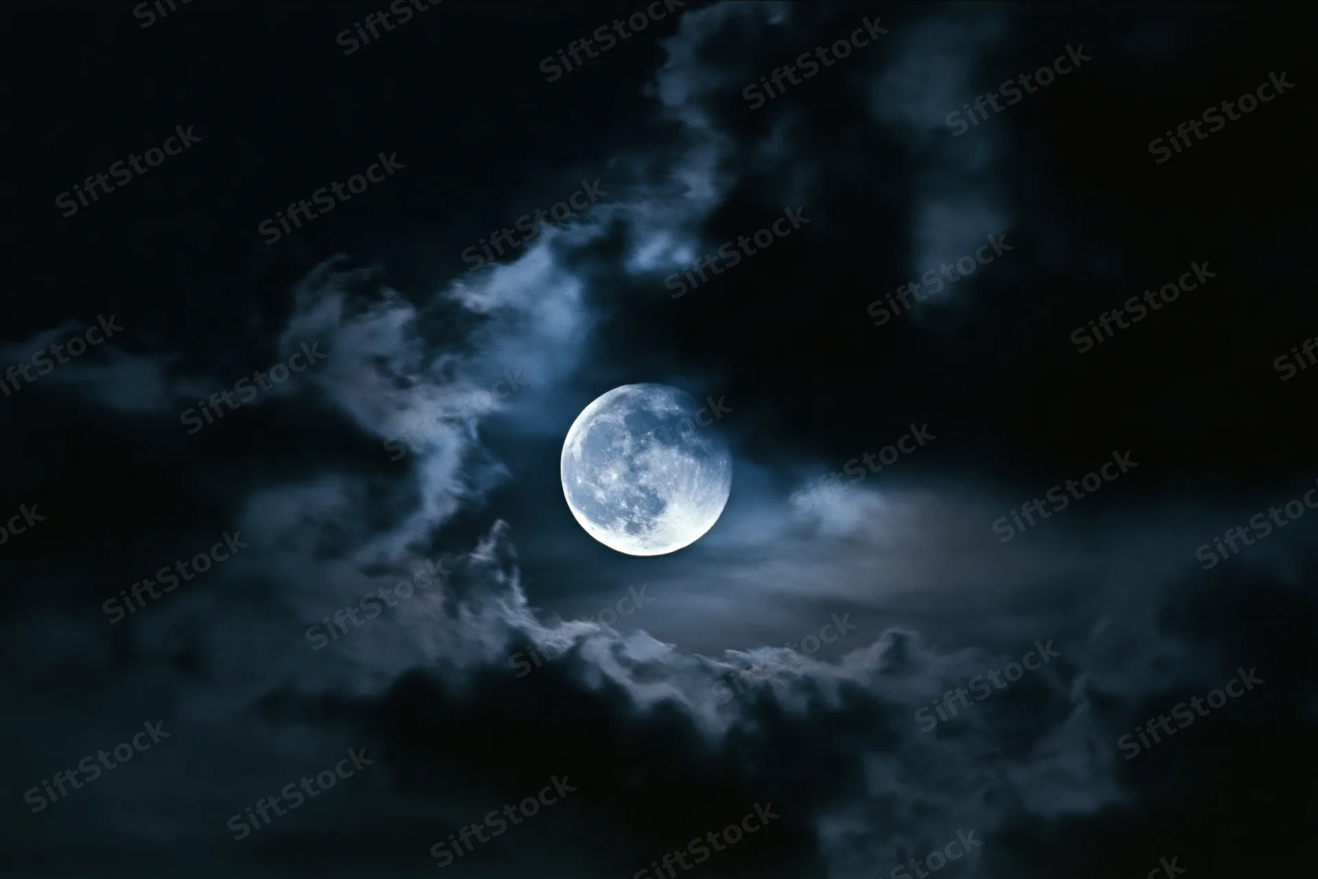 Full moon glowing through drifting dark clouds in the night sky