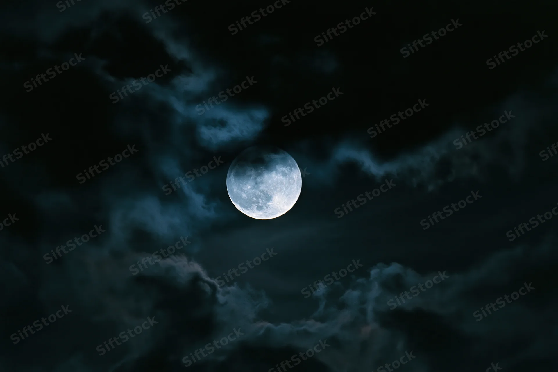 Full moon glowing in dark sky with drifting clouds around it