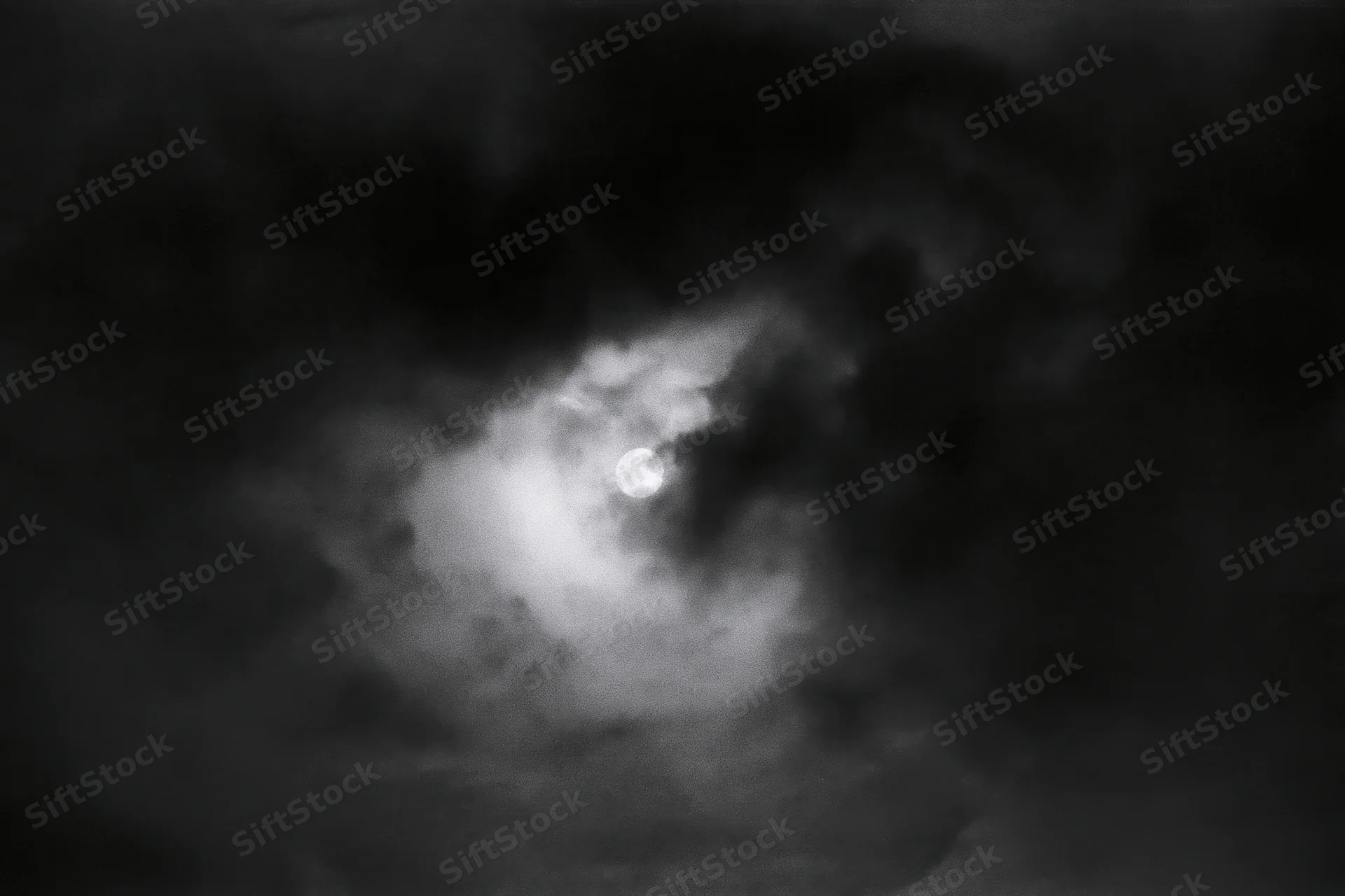 Full moon glowing through thick storm clouds in the night sky