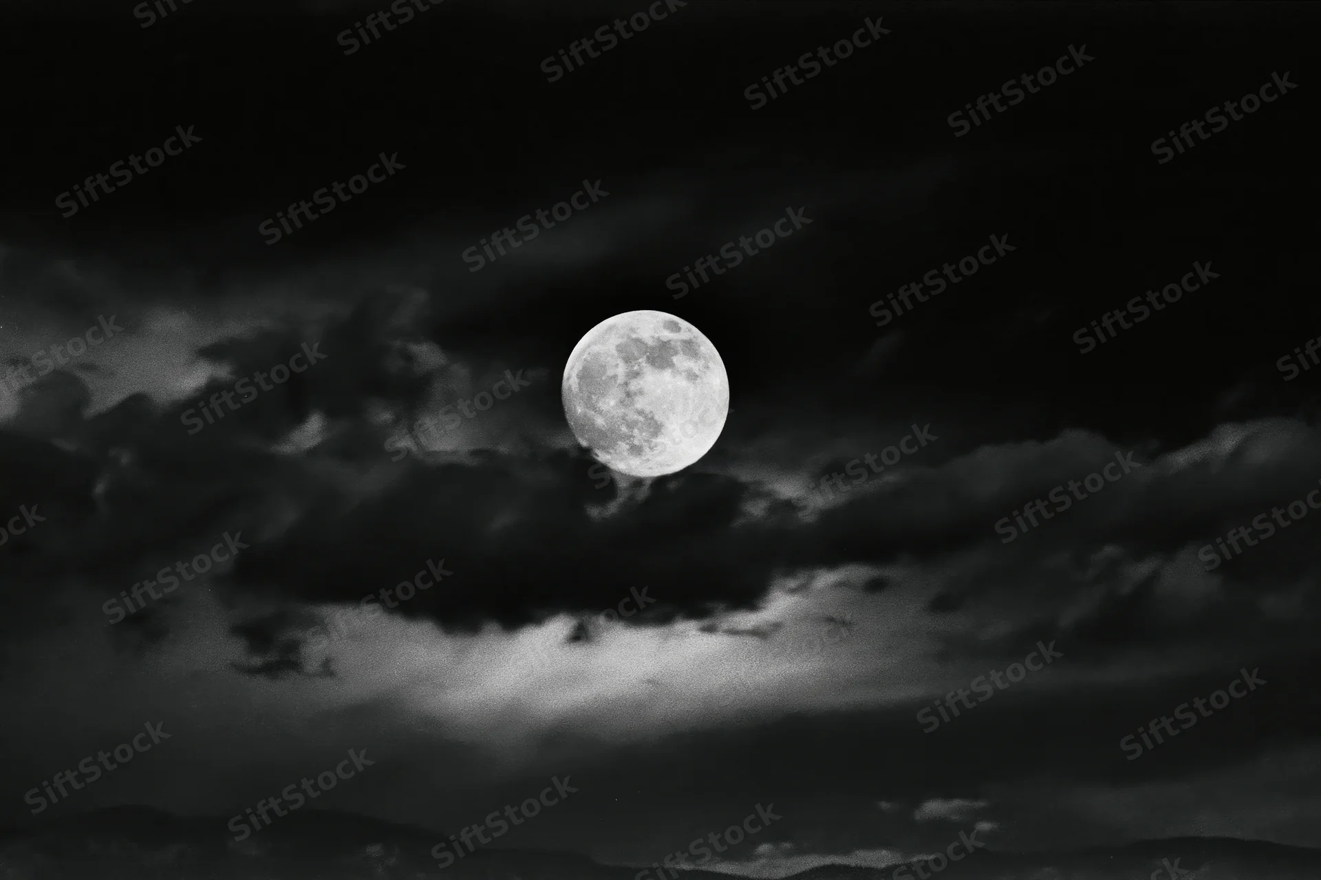Full moon glowing in dark stormy sky above distant mountains
