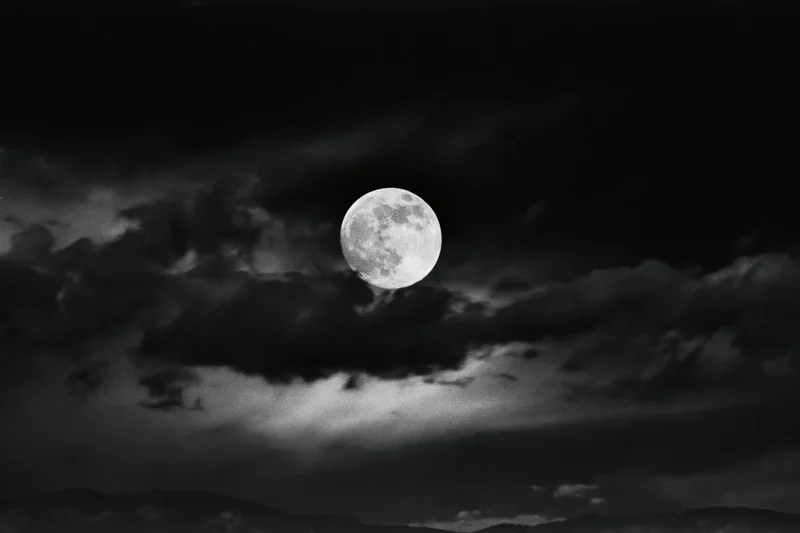 Full moon glowing in dark stormy sky above distant mountains