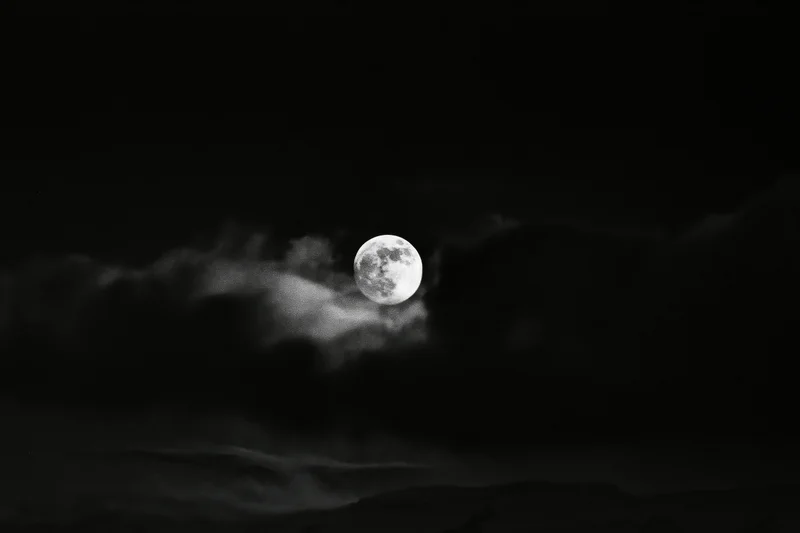 Full moon glowing through dark storm clouds in night sky
