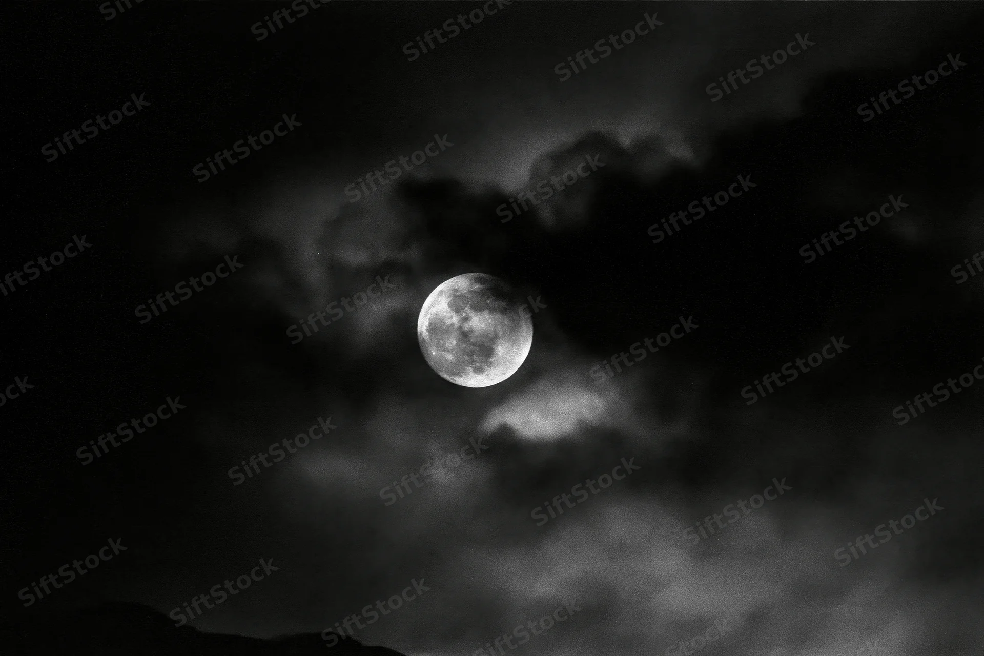 Full moon glowing through dark storm clouds above a silhouetted horizon at night