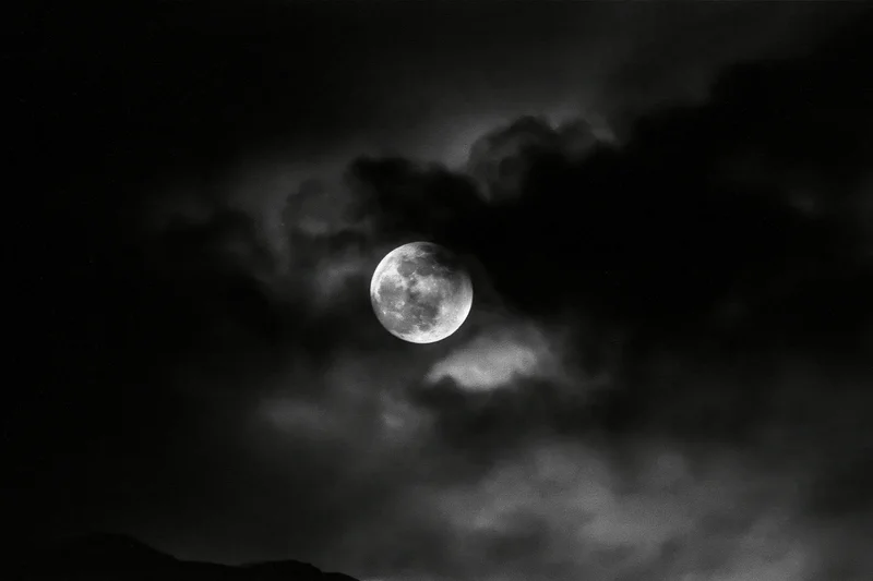 Full moon glowing through dark storm clouds above a silhouetted horizon at night